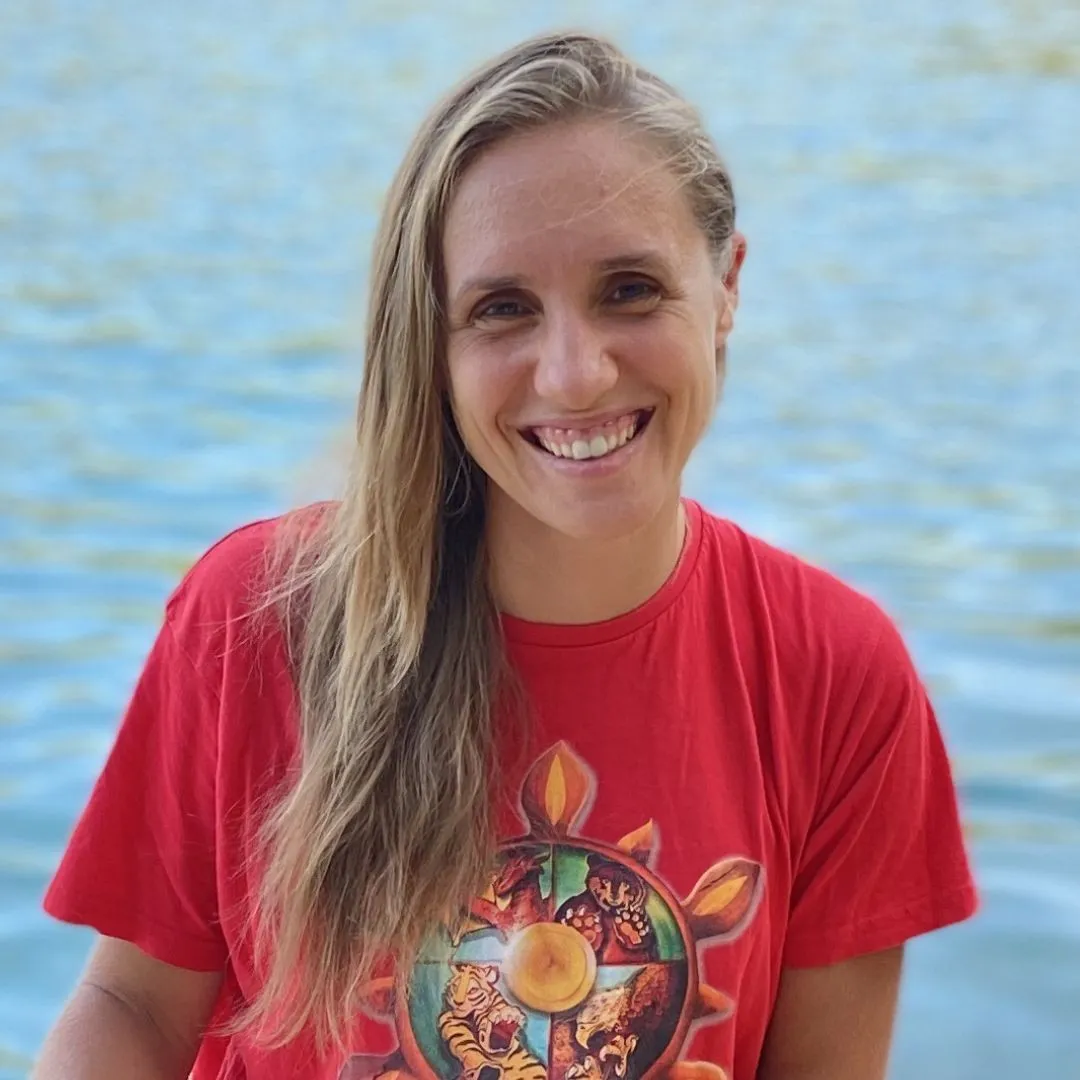 Santina Farago lächelt in die Kamera, im roten SanTi-Shirt mit dem Rad des Kung-Fu, im Hintergrund glitzerndes Wasser.