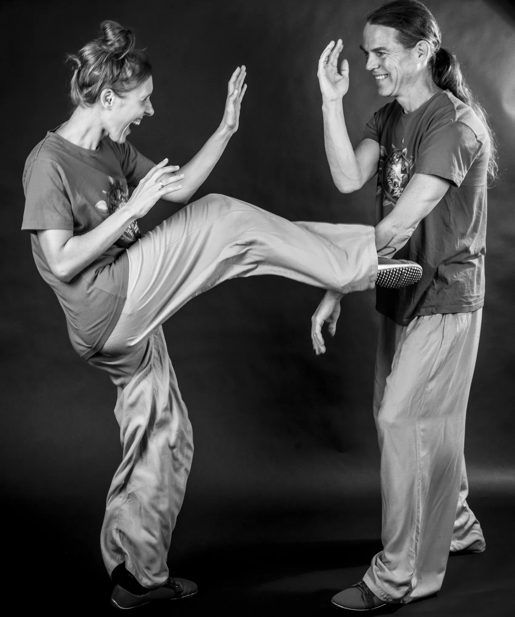 Schwarz-Weiß-Foto: Santina tritt lachend mit gestrecktem Bein, Tibor fängt ihren Fuß mit der Hand ab und lacht ebenfalls.