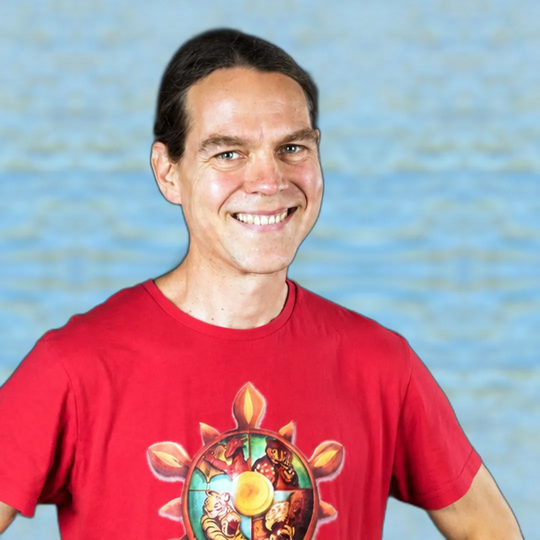 Tibor Farago lächelt in die Kamera, er trägt sein rotes Shirt mit dem Rad des Kung‑Fu, im Hintergrund Wasser.
